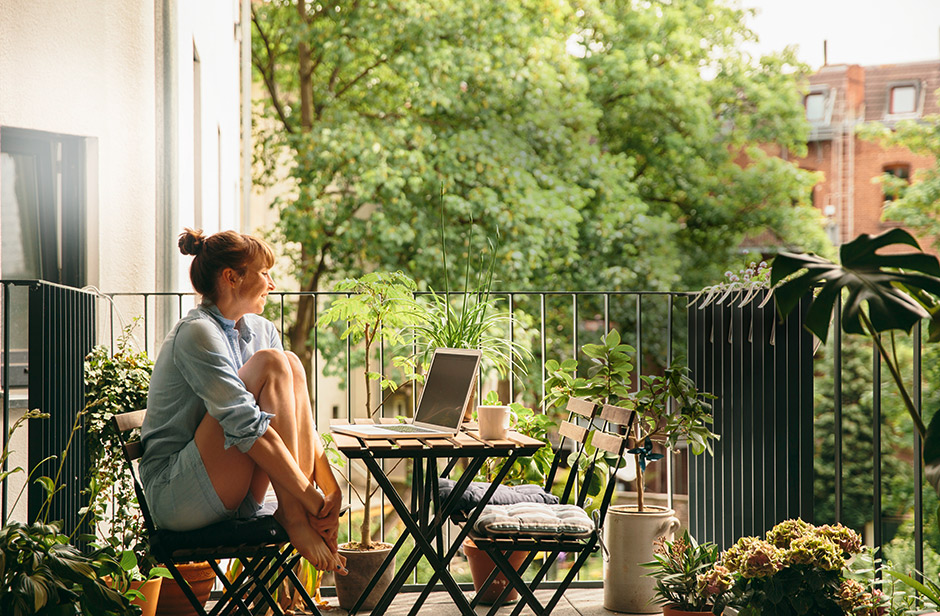 Eine Frau sitztmit dem Laptop auf der Terasse und genießt die Sonne.
